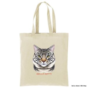 A beige tote bag features a realistic illustration of a gray tabby cat’s face with yellow eyes. Below the cat’s face, the words “BELLA GATTI” are printed in red uppercase letters. The background is plain white.