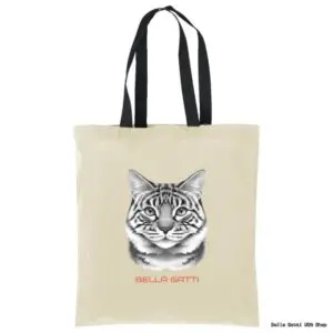 A beige tote bag with black handles features a realistic black-and-white drawing of a tabby cats face. Below the cat, red text reads “BELLA GATTI.” The background is plain white.