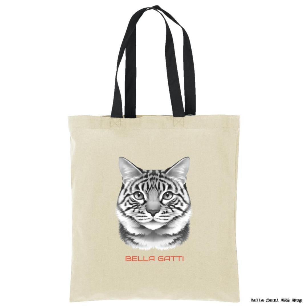 A beige tote bag with black handles features a realistic black-and-white drawing of a tabby cats face. Below the cat, red text reads “BELLA GATTI.” The background is plain white.
