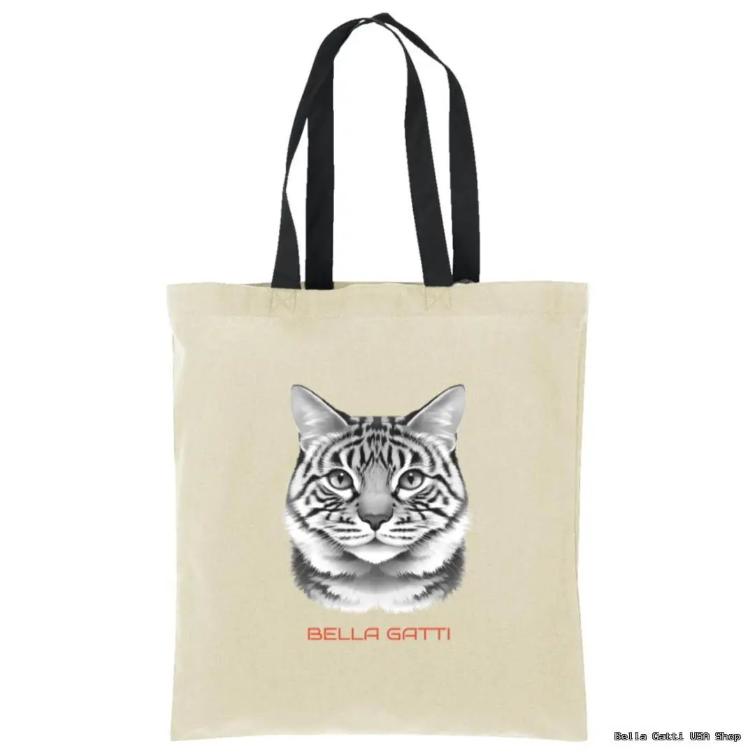 A beige tote bag with black handles features a realistic black-and-white drawing of a tabby cats face. Below the cat, red text reads “BELLA GATTI.” The background is plain white.