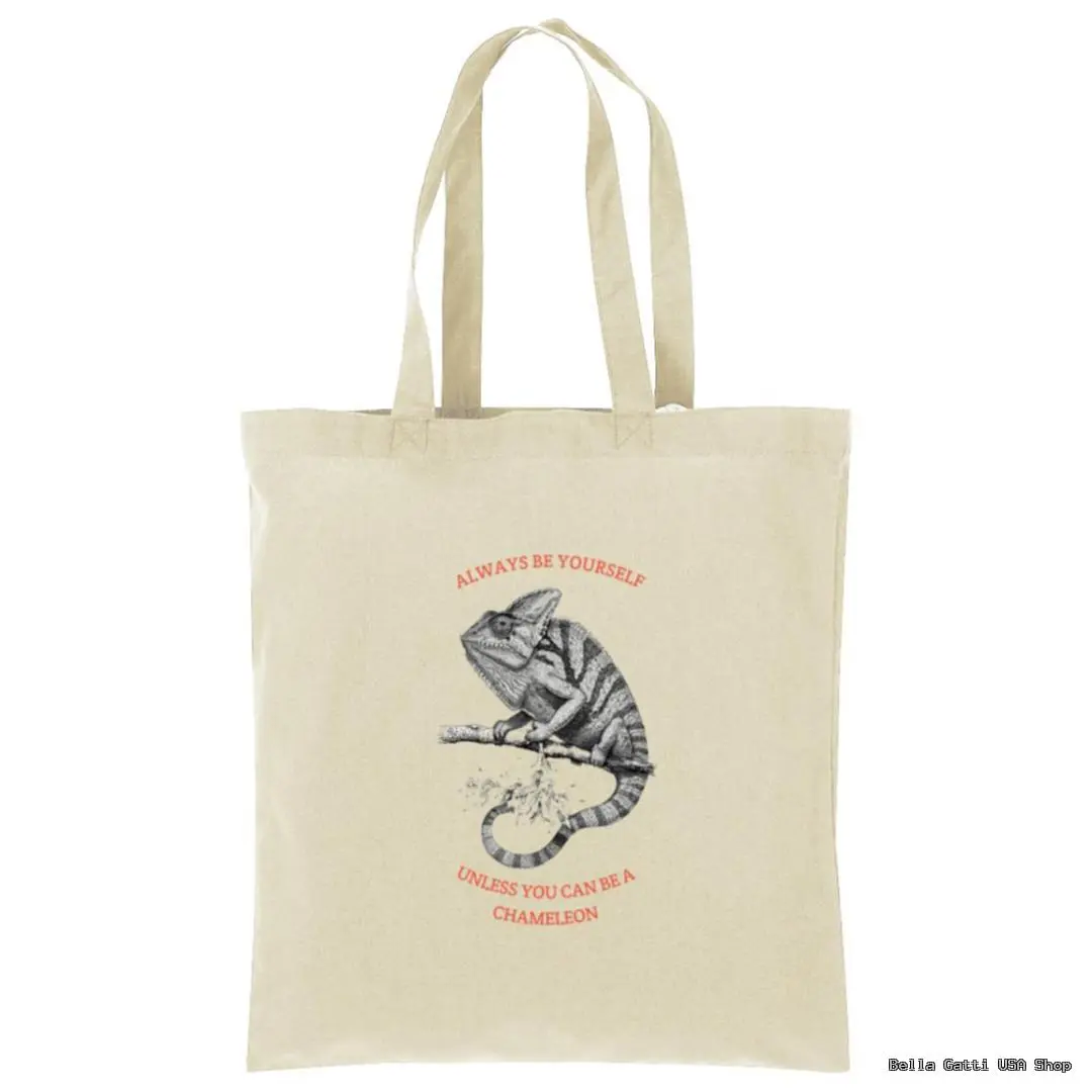 A beige canvas tote bag features a black and white sketch of a chameleon on a branch. Above and below the chameleon, red text reads: ALWAYS BE YOURSELF UNLESS YOU CAN BE A CHAMELEON. The bag has two handles.