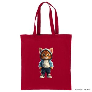 A red tote bag features an illustration of a cute, realistic orange kitten standing upright, wearing a blue hoodie, white shirt, dark pants, and sneakers. The kittens big eyes and casual outfit give it a playful, urban look.