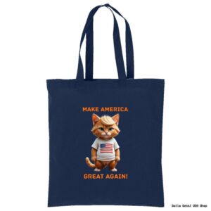 A navy blue tote bag features a cartoon orange cat wearing a white shirt with an American flag. Above and below the cat, orange text reads “MAKE AMERICA GREAT AGAIN!” The bag has long handles for carrying.