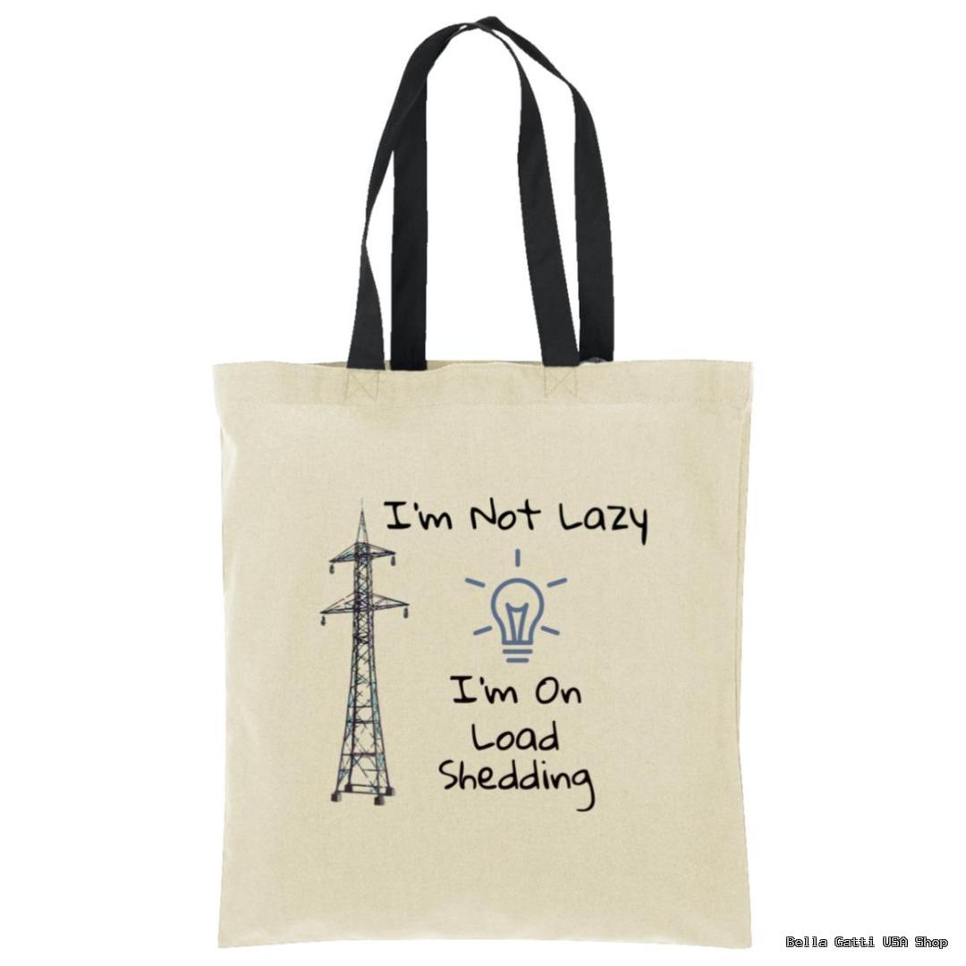 A beige tote bag with black handles features a drawing of an electricity pylon and a light bulb. Text reads: “I’m Not Lazy, I’m On Load Shedding.” The design humorously references power outages.