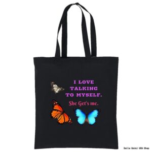 A black tote bag with two butterflies, one orange and black, one blue. White and pink text reads: I LOVE TALKING TO MYSELF. She Gets me. The design is centered and vibrant, with the butterflies flanking the text.