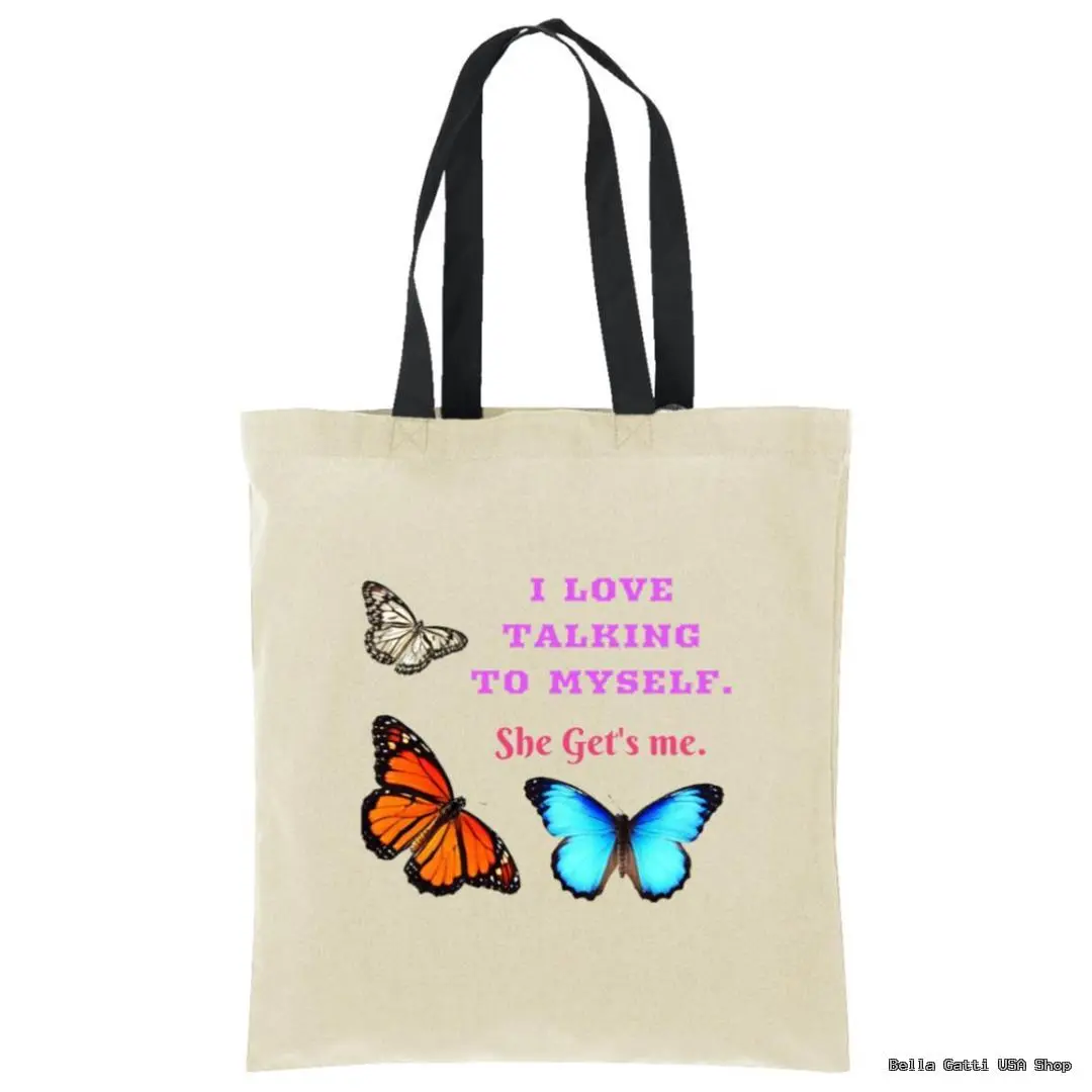 A beige tote bag with black handles features the text “I LOVE TALKING TO MYSELF. She Gets me.” in pink and purple. Three butterflies—one brown, one orange, and one blue—are pictured below and above the text.