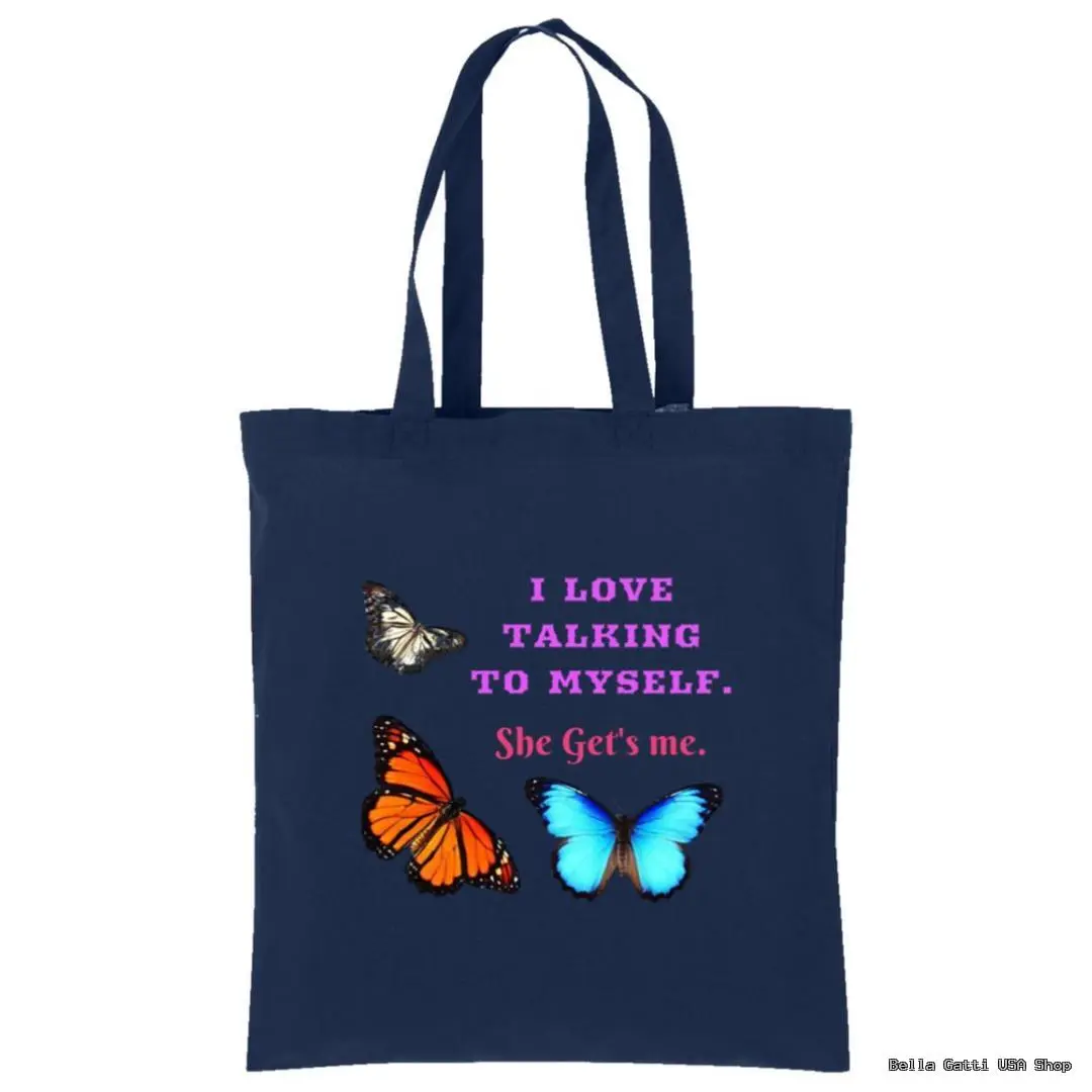A navy blue tote bag features two large, colorful butterflies—one orange and one blue—alongside a smaller brown butterfly. In the center, pink and white text reads, “I LOVE TALKING TO MYSELF. She Gets me.” The bag has two handles.