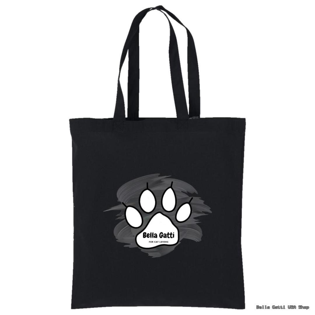 A black tote bag with two long handles features a large white paw print in the center. Inside the paw print is the text Bella Gatti in black uppercase letters, with FOR CAT LOVERS in smaller text underneath. A gray brushstroke background accents the paw print.