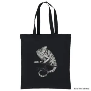 A black tote bag features a detailed grayscale illustration of a chameleon perched on a branch. The chameleon is facing left, and its curled tail and textured skin stand out against the dark background.