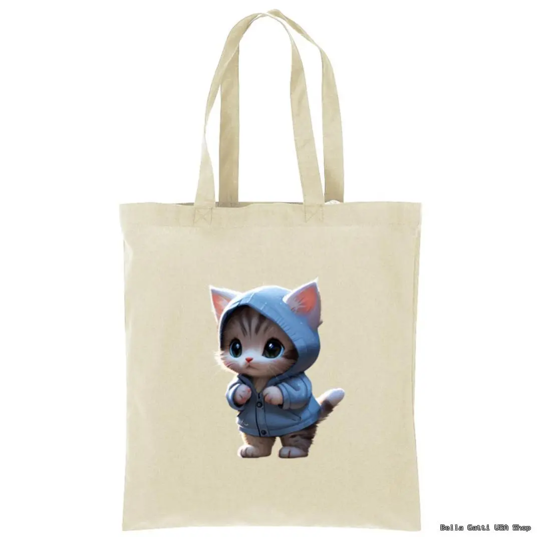 A beige tote bag featuring a printed illustration of a cute, wide-eyed kitten wearing a blue hoodie, standing upright on its hind legs with its front paws raised as if adjusting the hood. The background is plain and the design is centered.