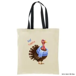 A beige tote bag with black handles features an illustration of a turkey wearing a blue scarf. Next to the turkey, the words Cold TURKEY are written in blue and orange playful fonts. The background is plain.