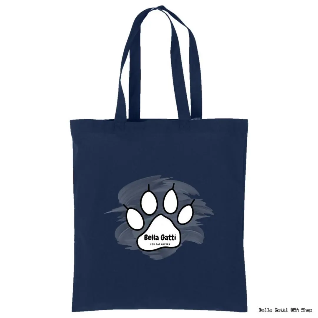 A navy blue tote bag features a large white cat paw print graphic in the center with the words “Bella Gatti for cat lovers” written in black on the paw pad, all set against a soft gray paint stroke background. The bag has two long handles.